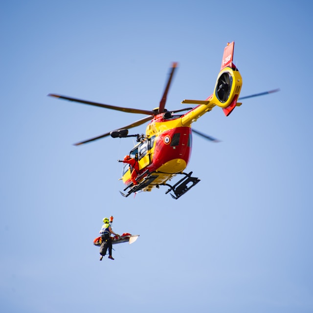 Red and yellow mountain rescue helicopter airlifting a person on a stretcher. Photo by Dion on Unsplash